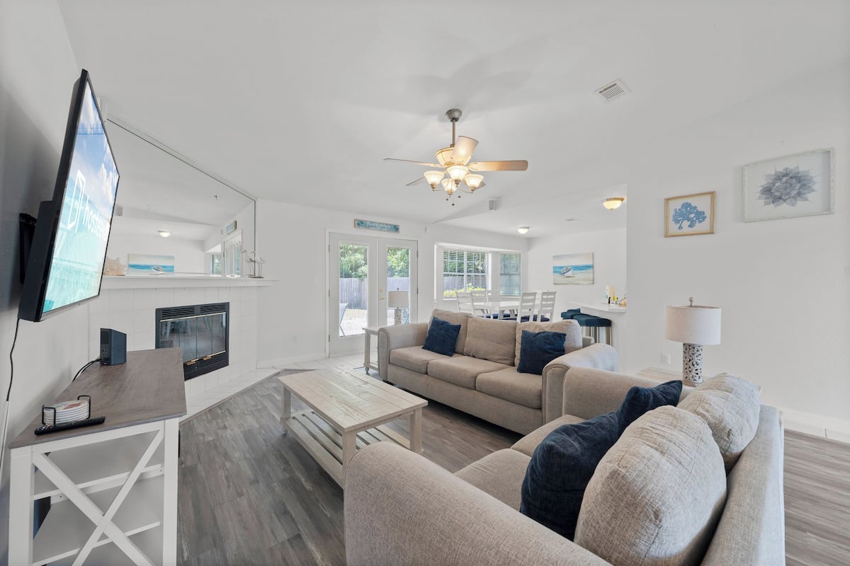 A modern living room with a sofa, coffee table, and TV. There is a fireplace, ceiling fan, and artwork on the walls.