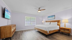 A bedroom with a bed, bedside tables, a TV, a ceiling fan, and a window. - Tranquil Haven | Pet Friendly (Pensacola)