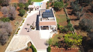 Vue aérienne d’une maison dotée d’un toit équipé de panneaux solaires, d’une piscine et d’un jardin aménagé.