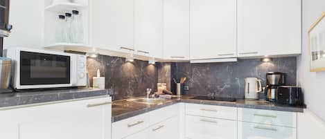 A modern kitchen with white cabinets, a microwave, a coffee maker, and a marble backsplash.