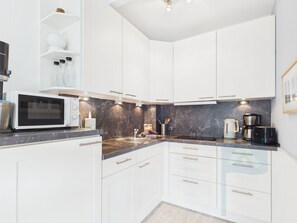 Una cocina moderna con armarios blancos, microondas, cafetera y salpicadero de mármol.