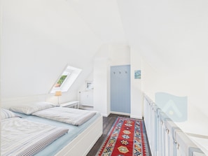 Une chambre à coucher avec un lit, une fenêtre, un radiateur, une porte et un couloir.