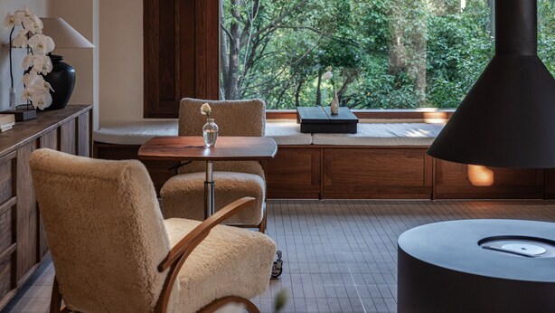 Ein modernes Interieur mit einem großen Fenster, Holzbalken, einem runden Tisch und einer Couch.