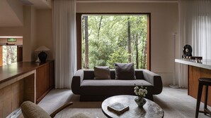 Ein modernes Wohnzimmer mit einer Couch, einem Couchtisch und Blick auf einen Wald durch ein großes Fenster.