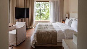 Ein Hotelzimmer mit Bett, Fernseher, Sessel und einem Fenster mit Vorhängen.