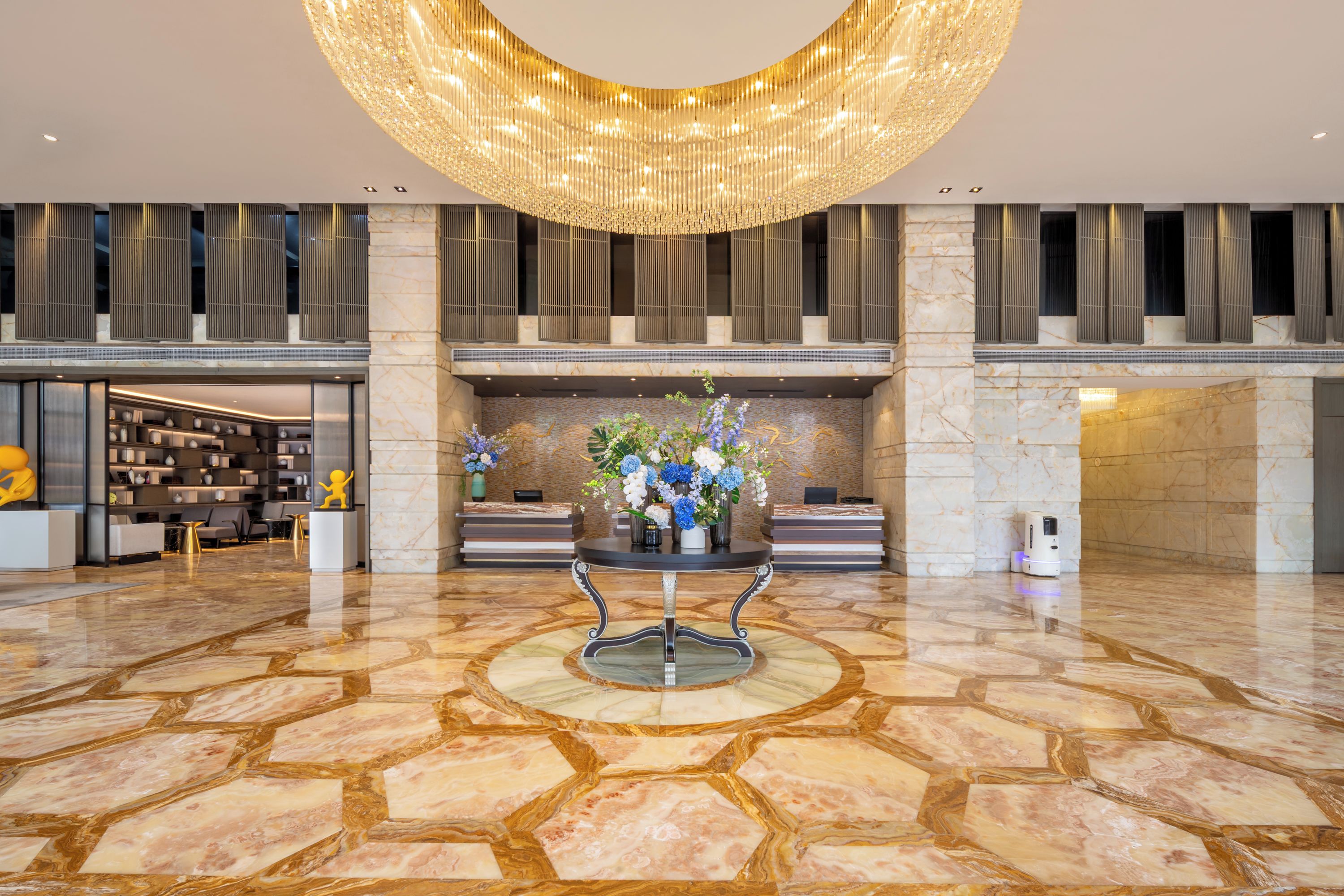 Um hall amplo com piso de mármore, um balcão de recepção e um grande lustre.