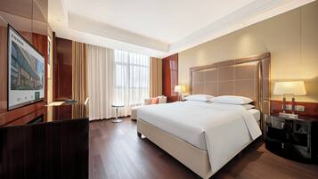 A hotel room with a large bed, a desk, a chair, a nightstand, and a window with curtains.