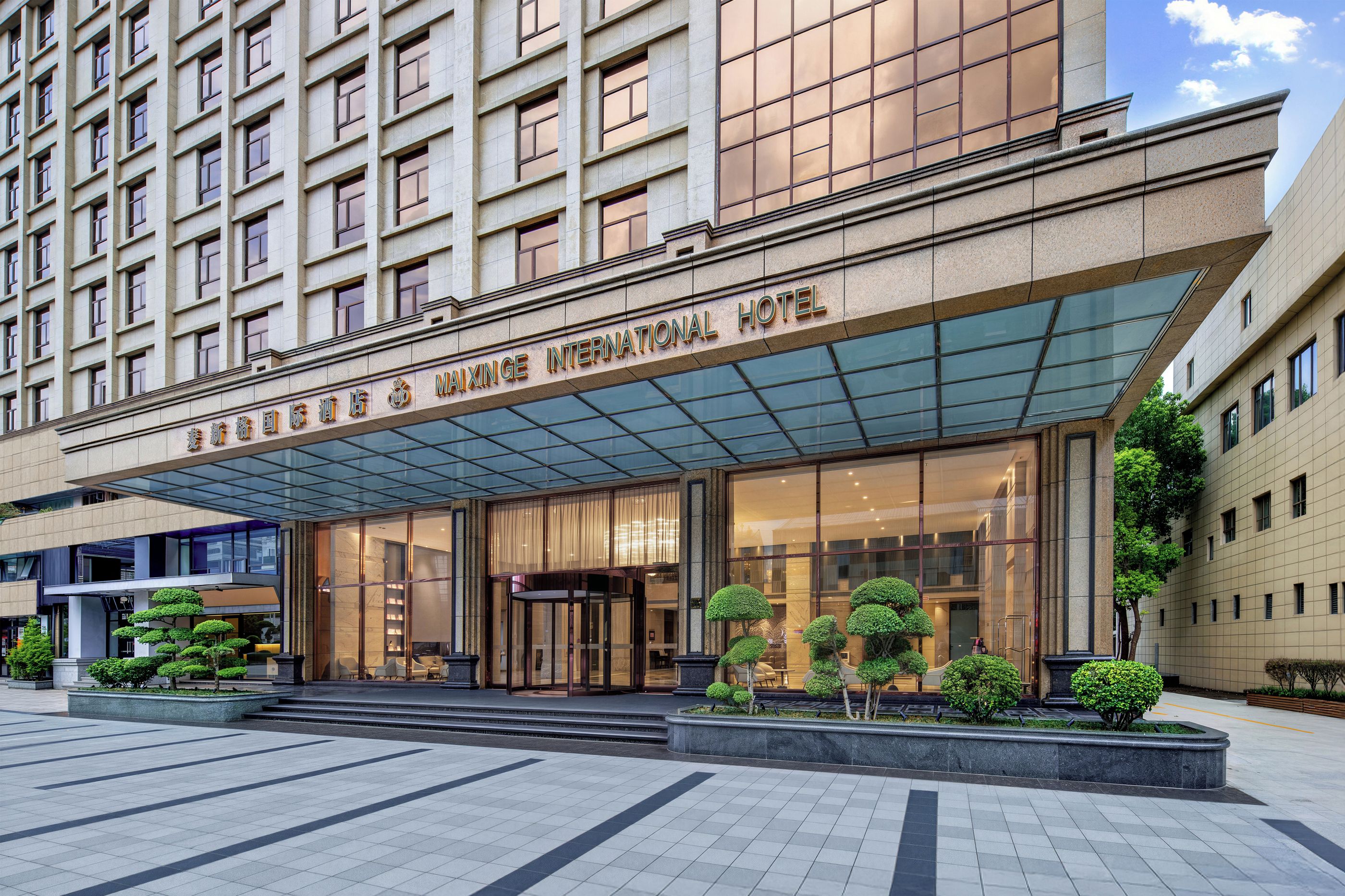 A hotel entrance with a glass canopy, a modern facade, and a well-maintained outdoor area with planters.