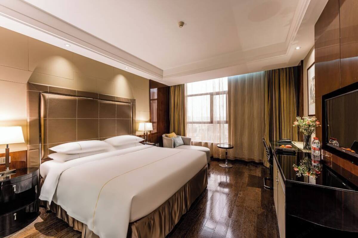 Une chambre d’hôtel avec un grand lit, un bureau avec une chaise, une télévision et une fenêtre avec des rideaux.