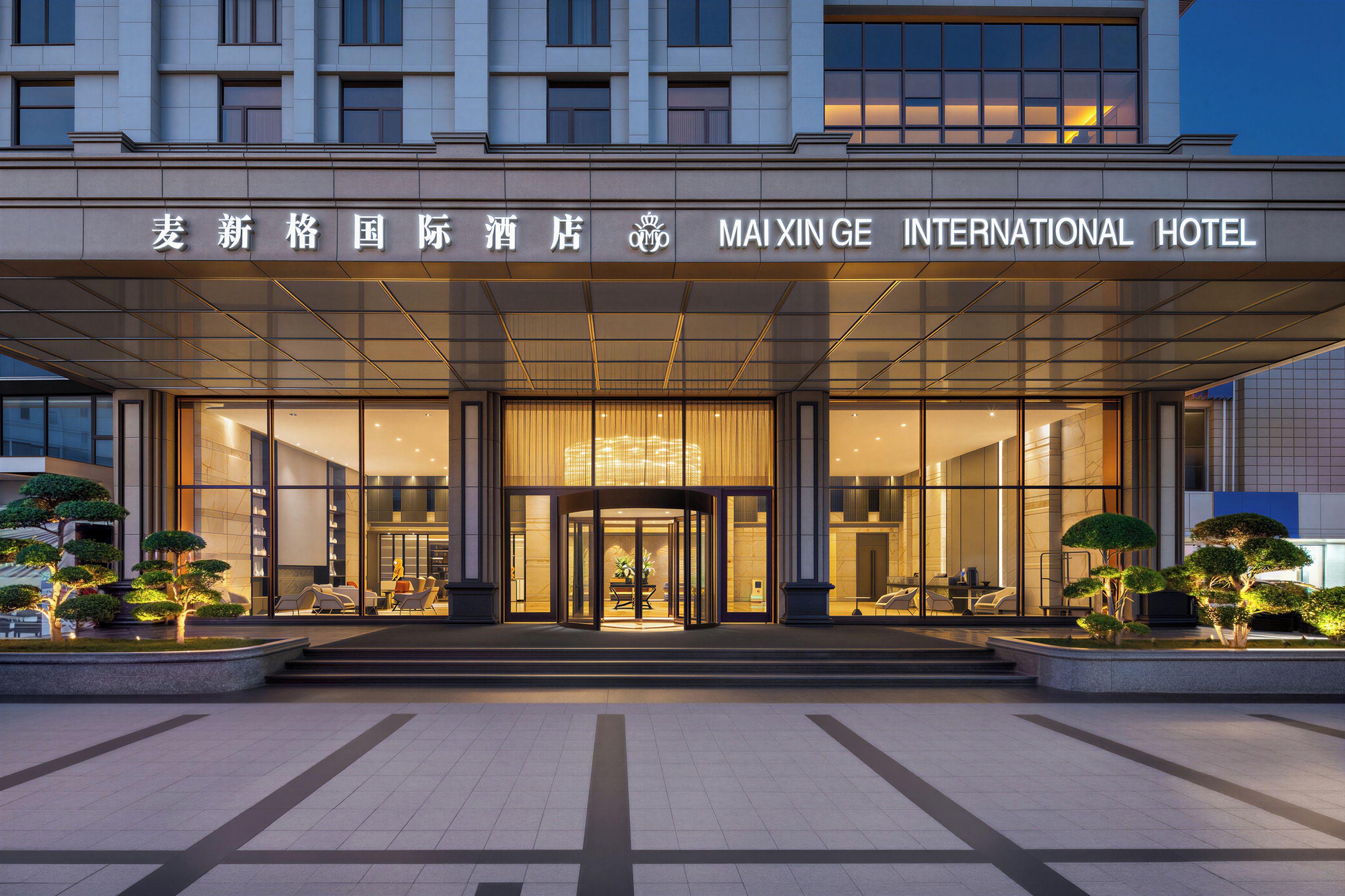 Indgangen til Maxingge International Hotel med en glasfacade, en central roterende dør og et symmetrisk design.