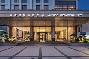 The entrance of the Maxingge International Hotel with a glass facade, a central revolving door, and a symmetrical design. - Mai Xinge International Hotel  (Shanghai)