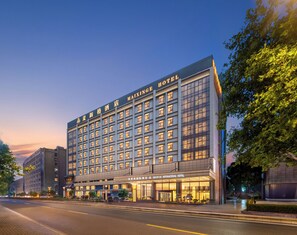 A multi-story hotel with a modern facade, large windows, and a prominent signage. - Mai Xinge International Hotel  (Shanghai)