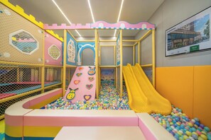Een kinderspeelplaats met een glijbaan, een bällebad en speelconstructies met netten.
