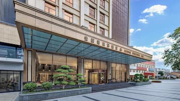 A modern hotel with a glass entrance, a well-maintained garden, and a clear sky.