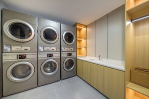 Un moderno cuarto de lavandería con cuatro lavadoras Haier, un lavamanos y armarios de madera.