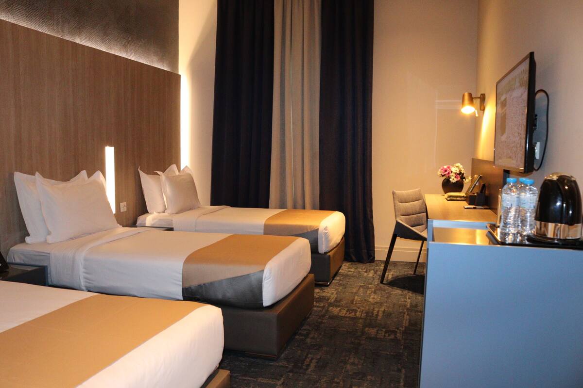 Een hotelkamer met twee bedden, een bureau met stoel, een koffiezetapparaat en een spiegel aan de muur.