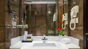 Une salle de bain moderne avec un mur en marbre, un grand miroir, un lavabo avec des articles de toilette et un espace douche.
