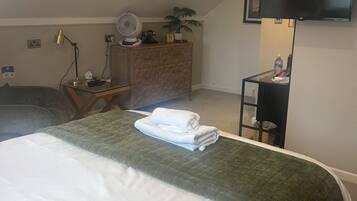 Habitación de hotel con cama, escritorio, silla, televisión y planta.