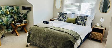 A bedroom with a bed, bedside tables, a desk, and a potted plant.