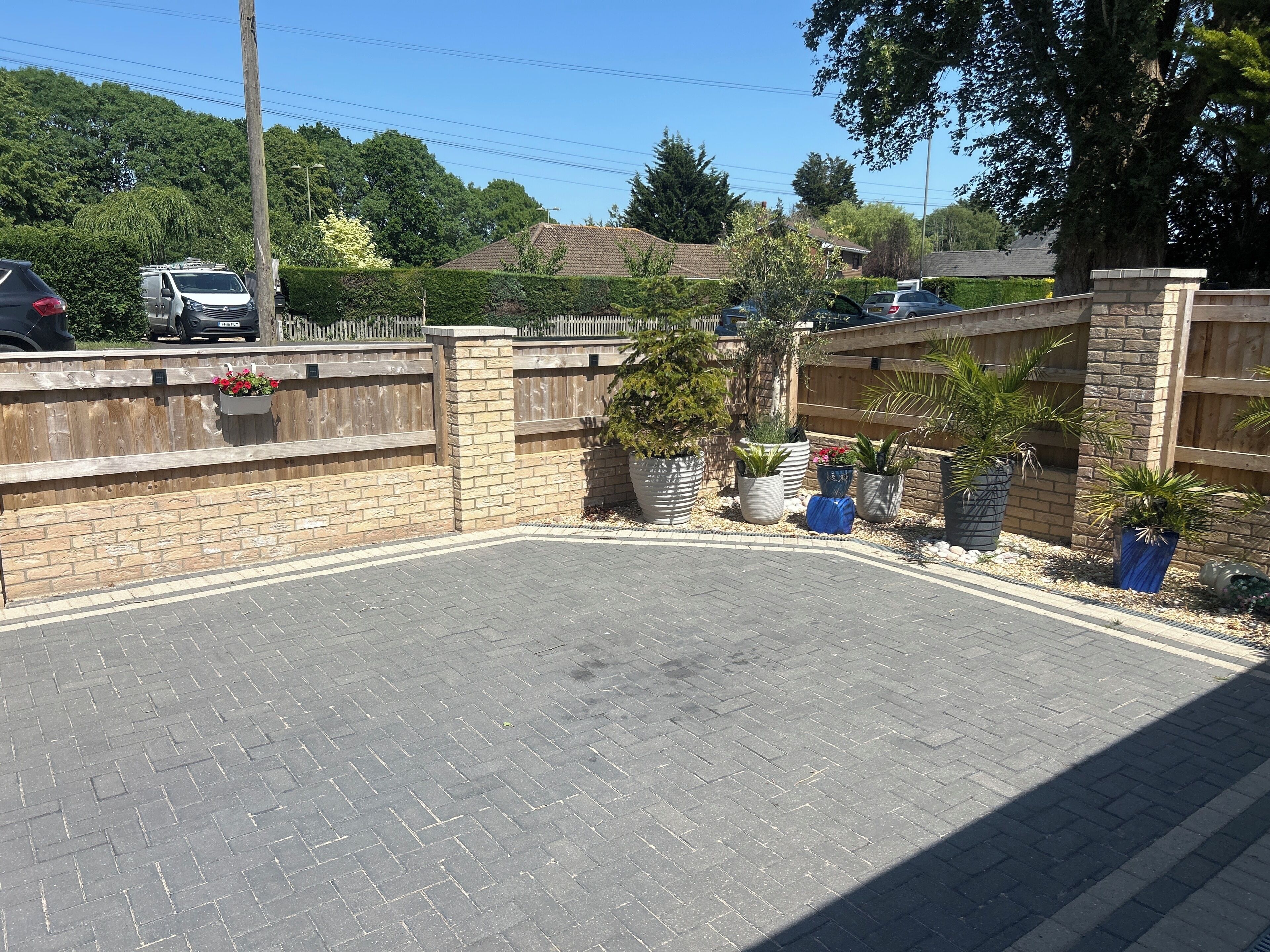 A paved parking area with a brick wall, potted plants, and a wooden fence.