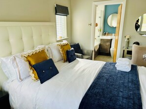 A neatly made bed with white and dark blue pillows, a blue blanket, and a small table with towels.