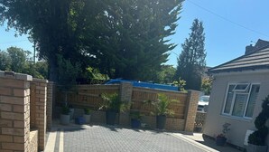 Un camino de entrada pavimentado con una rejilla metálica, rodeado de muros de ladrillo y plantas en macetas.