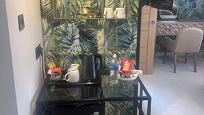 Una habitación compacta con una mesa de vidrio, una cafetera negra, una botella de agua y un cubo de basura.