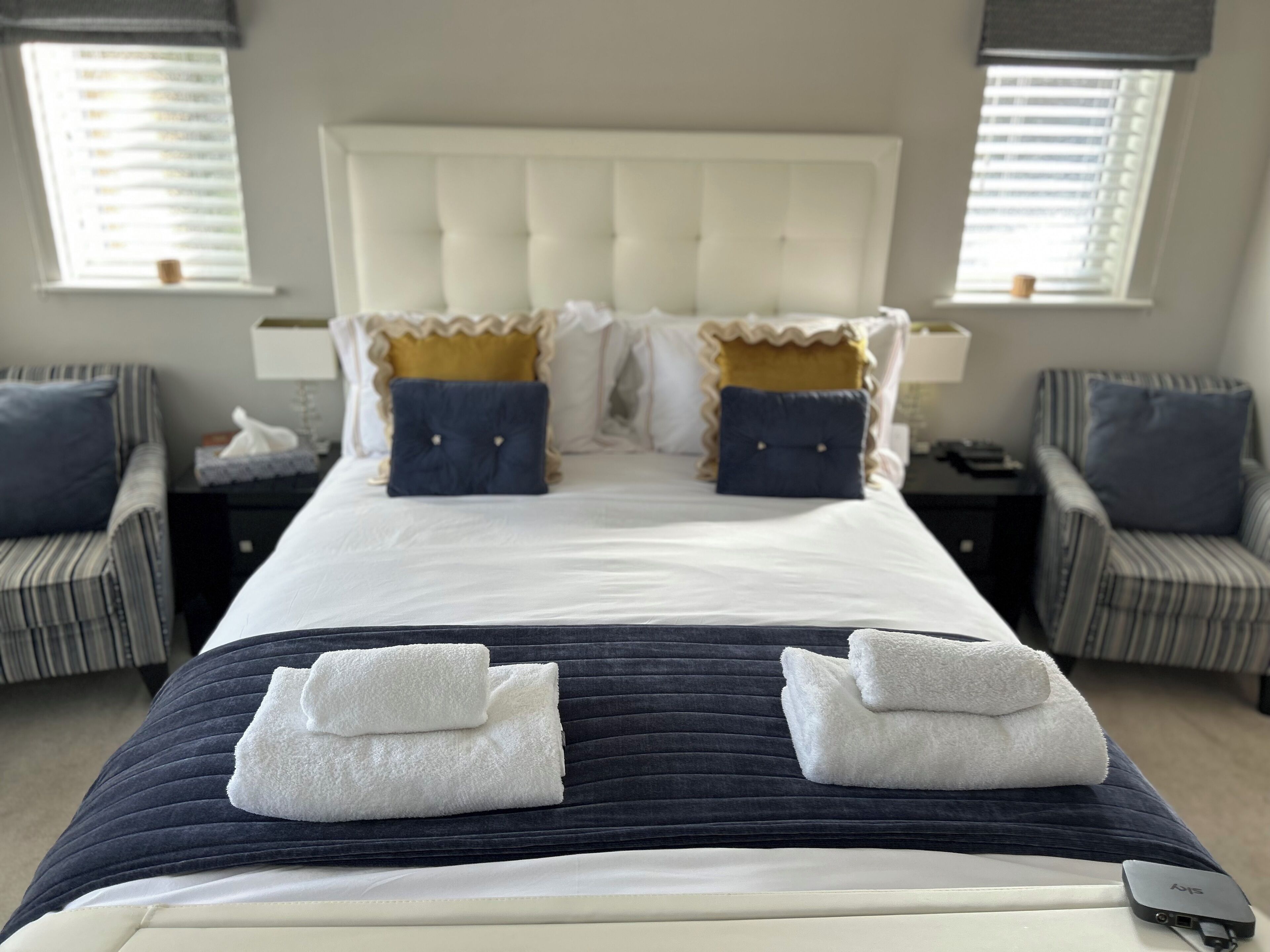 Habitación de hotel con una cama grande, dos mesitas de noche, una silla y una ventana con persianas.