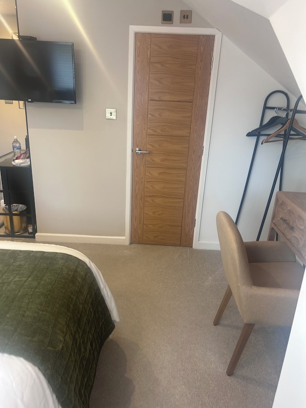 A bedroom with a bed, a chair, a wooden door, a coat rack, and a flat-screen TV.