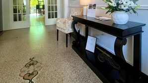 Un couloir avec une console noire, une chaise à motifs et un vase rempli de fleurs.