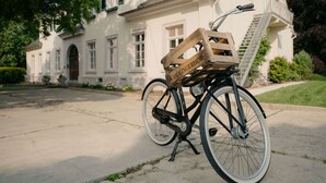 Un vélo avec une caisse en bois portant l’inscription « KARLINGERHOF » est garé devant un bâtiment blanc doté d’un escalier.