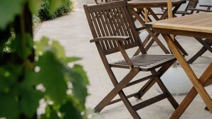Une terrasse extérieure avec des tables et des chaises en bois, des parasols blancs et une vue sur un bâtiment en arrière-plan.