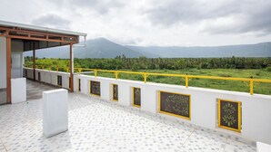 Una terraza con piso de baldosas y barandillas amarillas, con vistas a un paisaje verde y montañas.