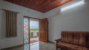 A room with a brown sofa, a wooden door with intricate carvings, and a view through a glass door with colorful patterns. - Luxury Service Apartment Near IshaYoga Coimbatore. Beautiful Mountien View Rooms (Madawarayapuram)
