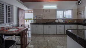 A modern kitchen with a marble countertop, white cabinets, and a ceiling fan. - Luxury Service Apartment Near IshaYoga Coimbatore. Beautiful Mountien View Rooms (Madawarayapuram)