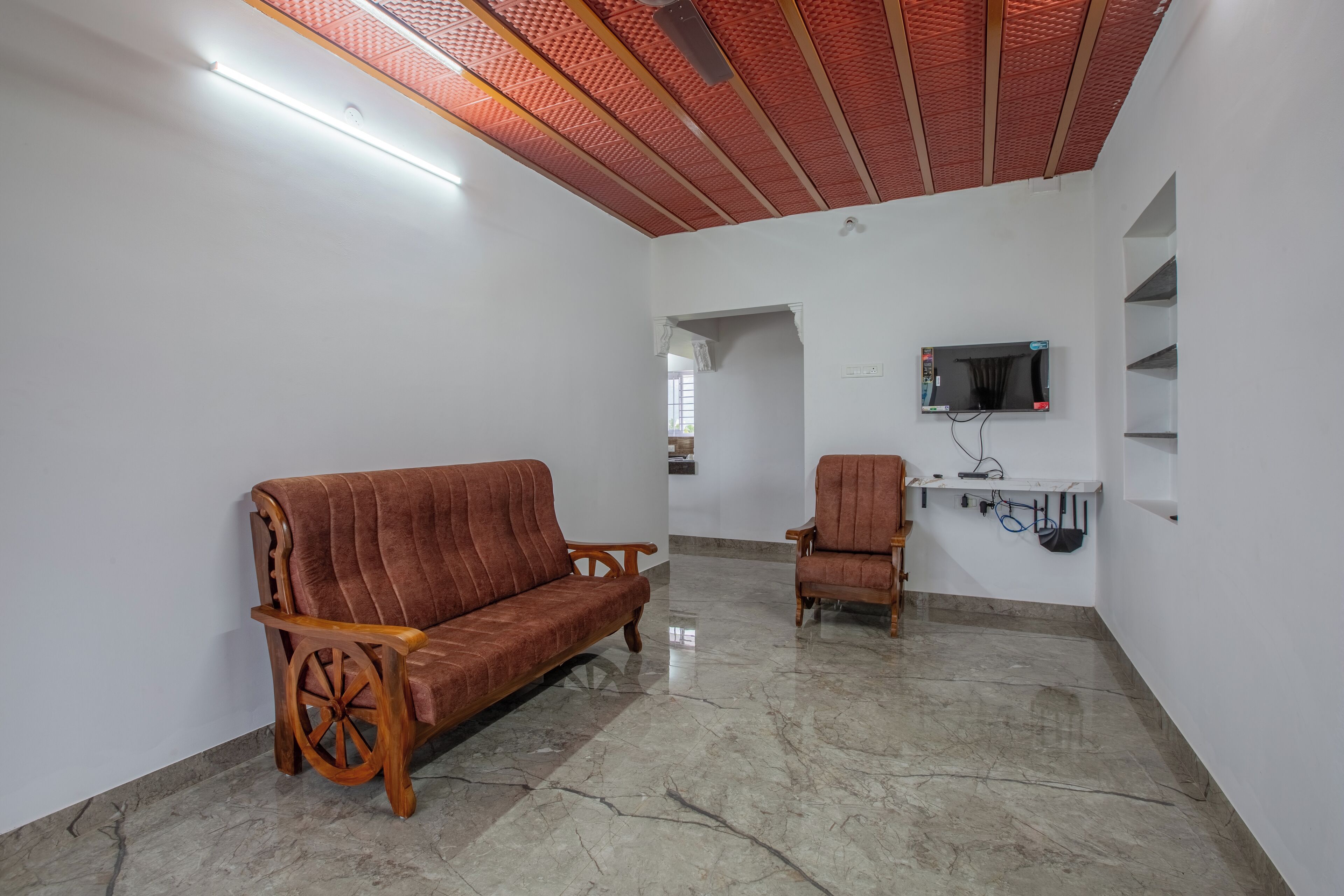 Ein Zimmer mit einer Holzsofa und Sesseln, einem flachbildfernseher an der Wand und einer Decke mit roten Dämmplatten.