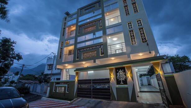 A multi-story building with a modern design, featuring a central entrance with a decorative gate and a staircase leading to the upper floors. - Luxury Service Apartment Near IshaYoga Coimbatore. Beautiful Mountien View Rooms (Madawarayapuram)