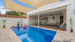 Una piscina con cerramiento de vidrio, un patio cubierto y vistas al espacio interior de la sala.