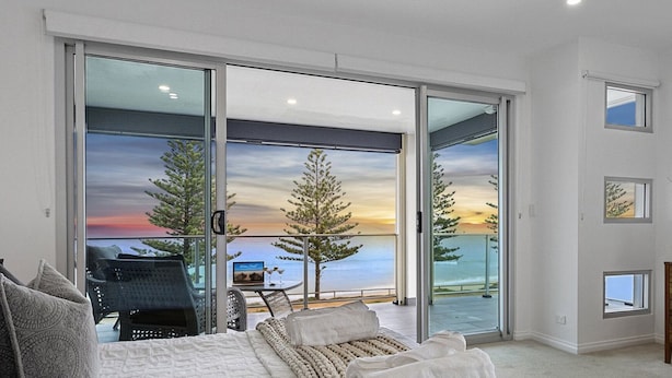 Un dormitorio con un amplio ventanal corredero que da a un balcón con vistas al mar y al atardecer.