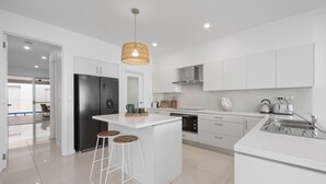 Una cocina moderna con muebles blancos, una isla central con taburetes, horno integrado y un lavamanos de acero inoxidable.
