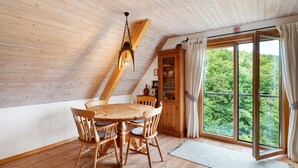Una mesa de comedor de madera con sillas, un aparador de madera con puertas de cristal y un ventanal con cortinas.