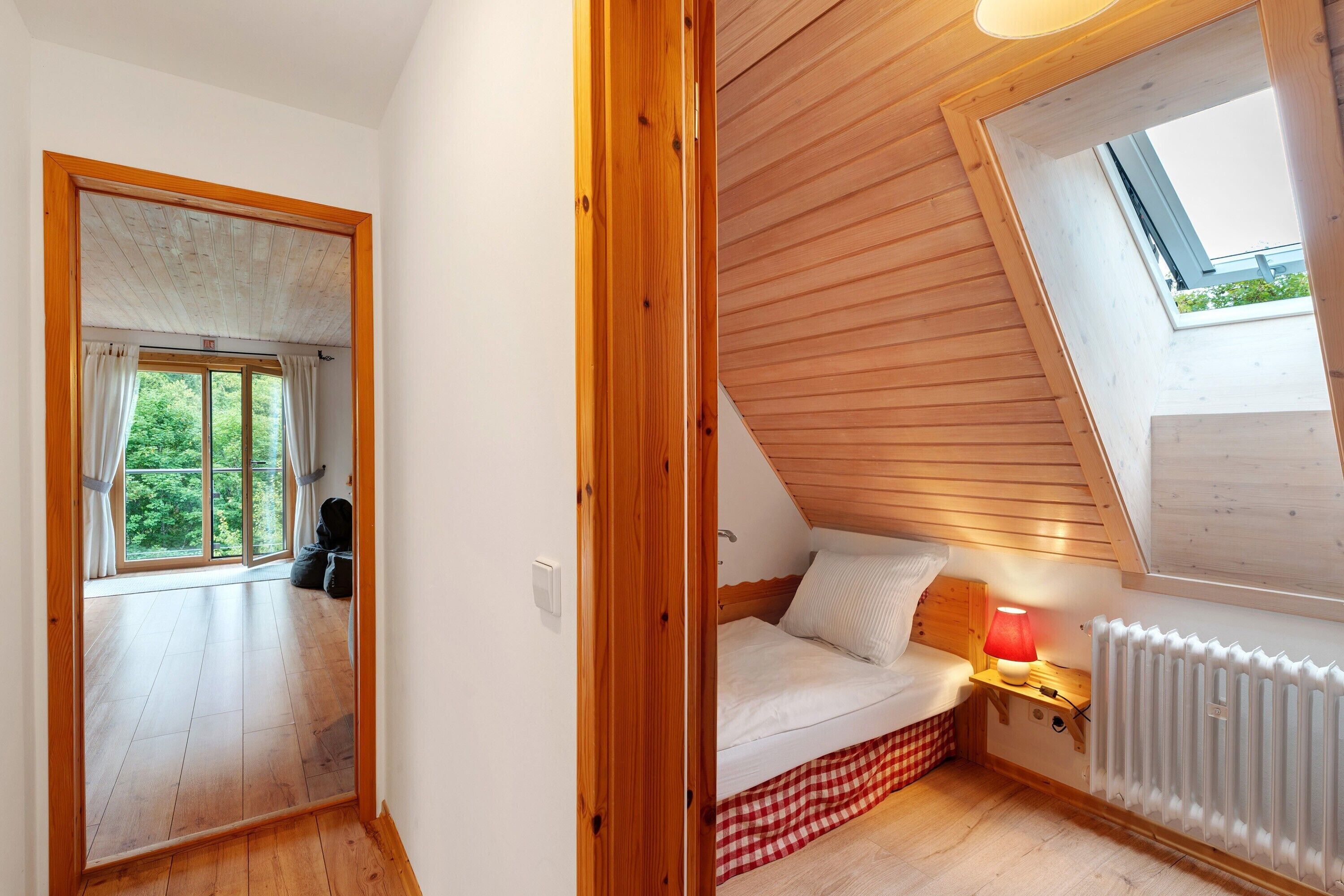 A room with a sloped ceiling, a bed, a radiator, and a window.