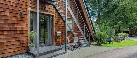 A modern building with a wooden exterior, a metal staircase, a mailbox, and a grassy area with a hammock.