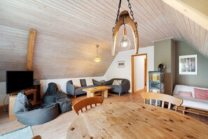 A loft-style room with a wooden ceiling, a TV, a sofa, a dining table, and bean bags.
