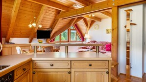 Un intérieur en bois comprenant un coin cuisine, un espace repas et un salon avec un canapé et un téléviseur.