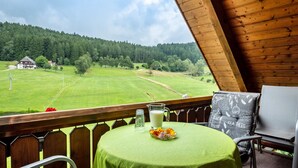 Un balcon avec une table, une chaise et une vue sur un champ verdoyant et une forêt.