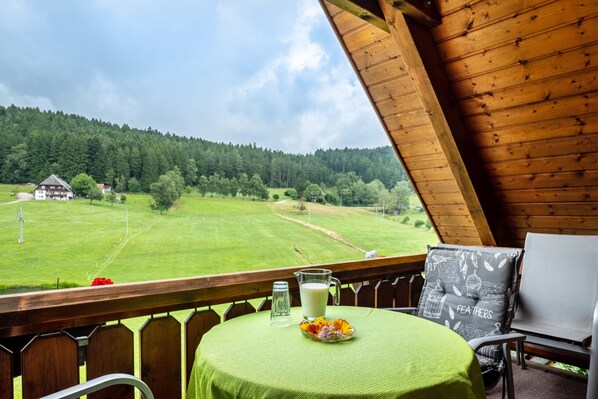 Un balcon avec une table, une chaise et une vue sur un champ verdoyant et une forêt.
