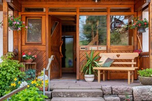 A wooden cabin entrance with a bench, potted plants, and a welcome sign.