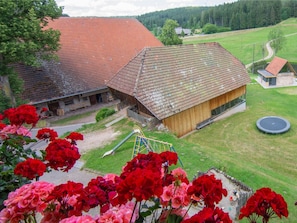 Une maison de campagne avec un toit recouvert de tuiles rouges, une grange en bois et un trampoline dans la cour.