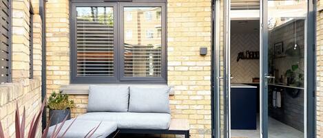 A modern outdoor seating area with a bench, a potted plant, and a sliding glass door leading to a kitchen.